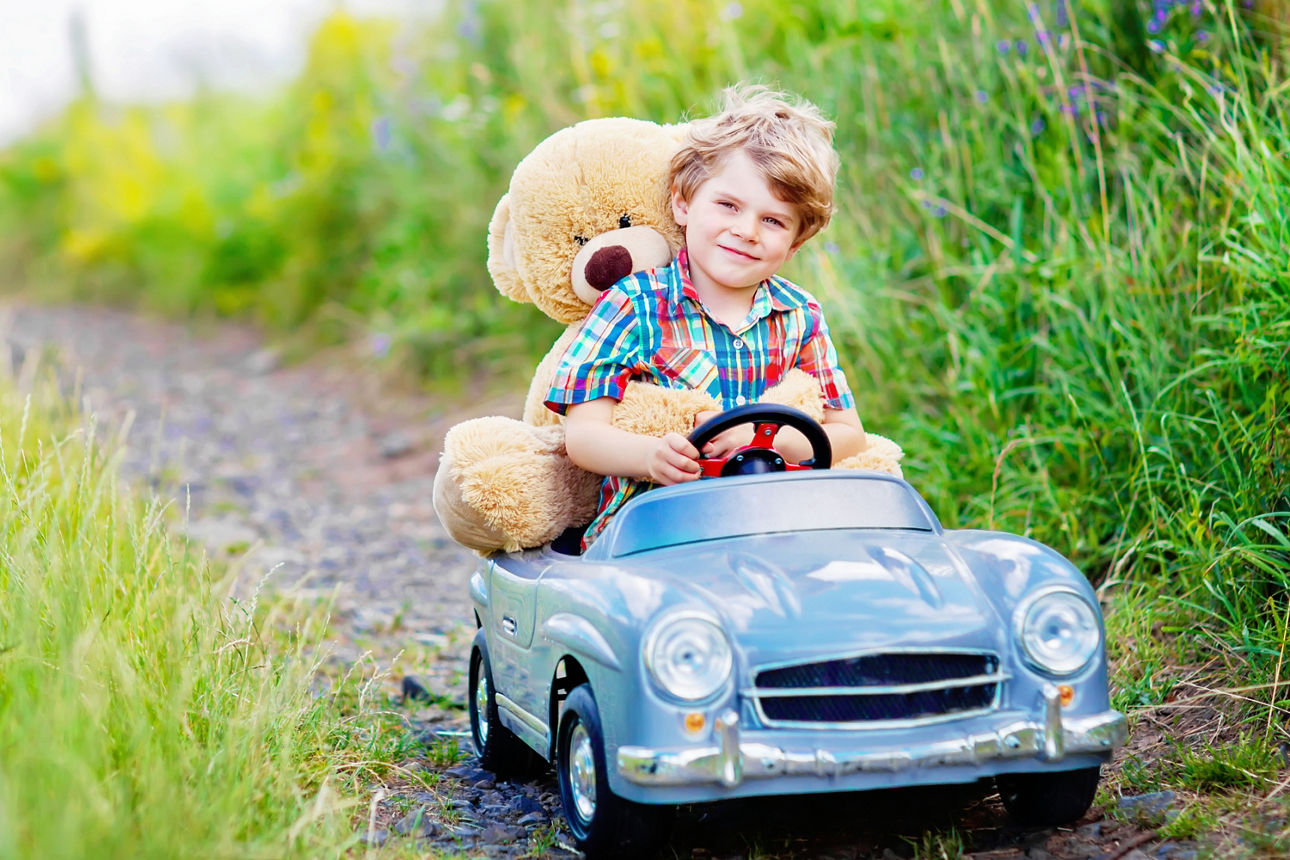 Ein keiner Junge mit einem Teddybär sitz in einem kleinen Auto