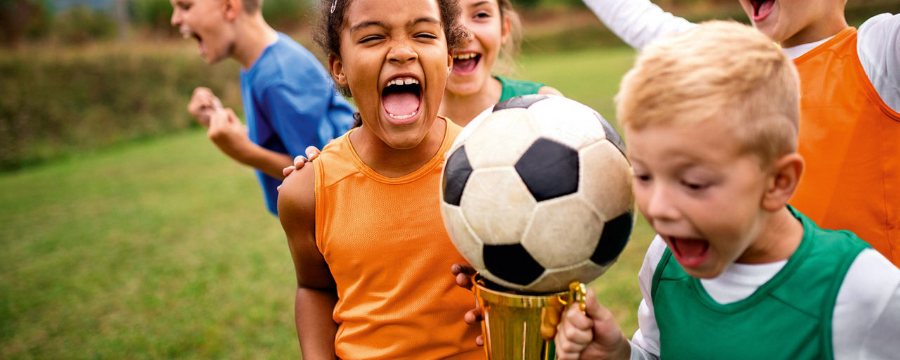 Kinder spielen Fussball und jubeln