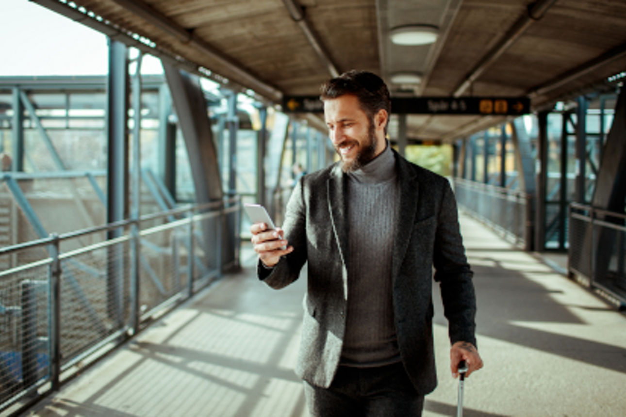 Mann auf einem Bahnhof mit Handy und Koffer in der Hand