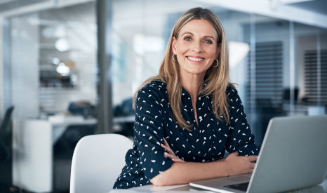Lächelnde Frau an einem Schreibtisch vor ihrem Laptop