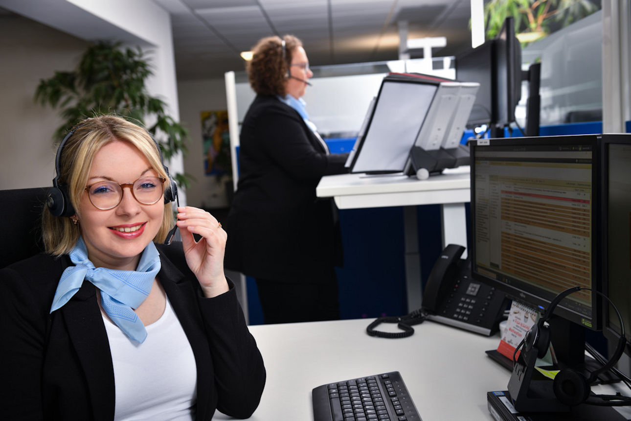 Junge Frau blickt in die Kamera, während eine weitere Kollegin im Hintergrund arbeitet