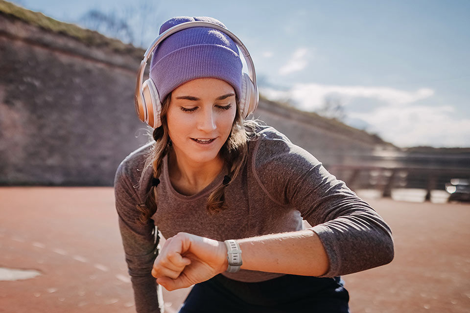 Junge Frau mit Kopfhörern schaut auf die Knie abgestützt nach einem Lauf auf Ihre Garmin Smartwatch