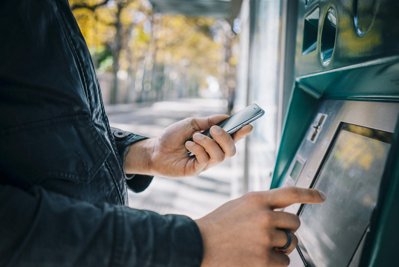 Person steht am Geldautomat mit Smartphone