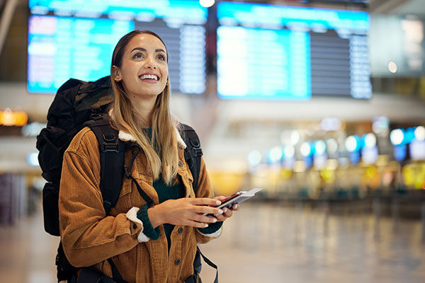 Junge Frau steht mit Gepäck und Reisepass in der Hand in der Schalterhalle eines Flughafens