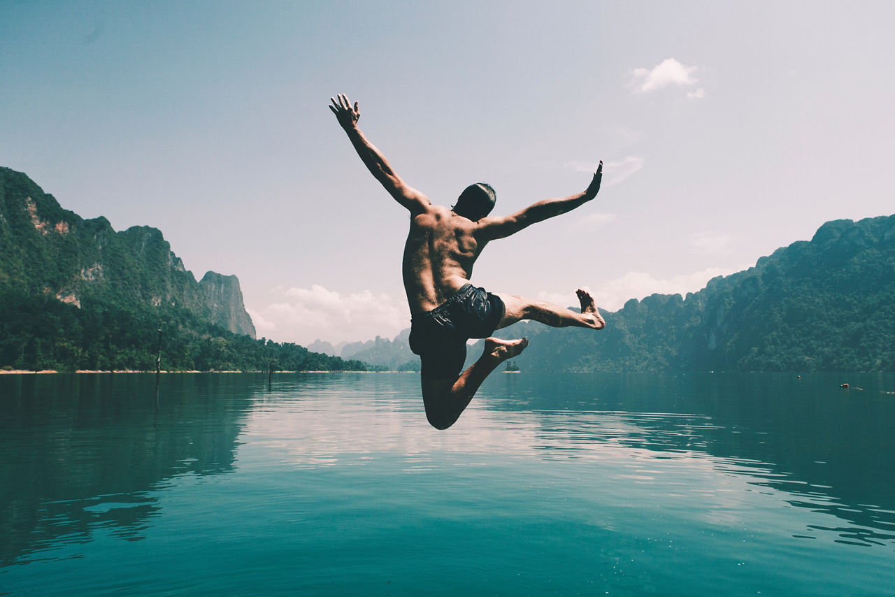 Ein Mann springt ausgelassen in einen Natursee. 