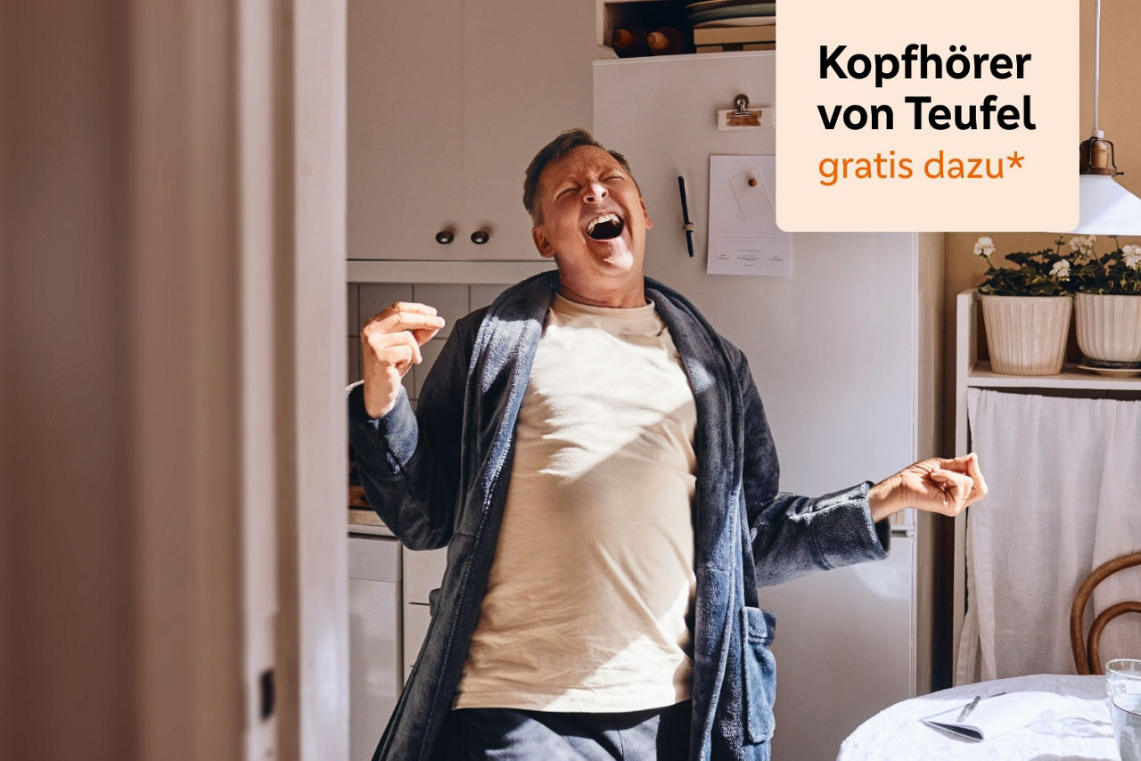 Mann singt glücklich im Bademantel in seiner Küche mit dem Hinweis "Kopfhörer von Teufel gratis dazu*"
