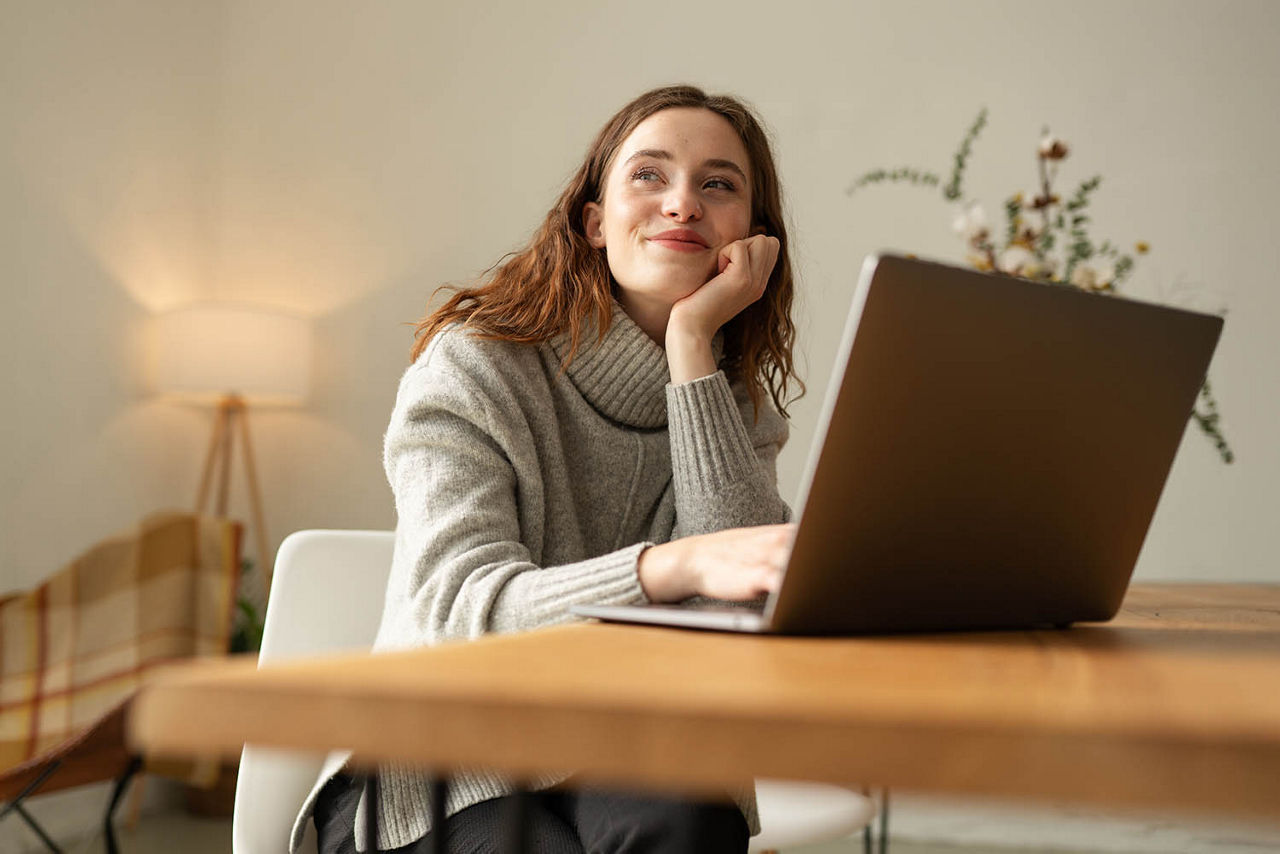 Junge Frau sitzt verträumt mit einem Lächeln an Ihrem Notebook
