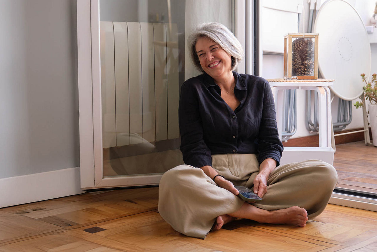 Frau sitzt im Schneidersitz auf dem Boden vor der offenen Balkontür
