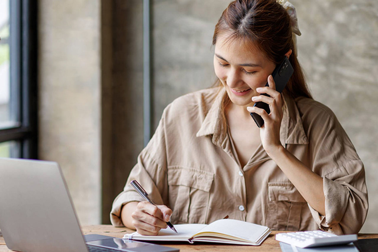 Junge Frau telefoniert und notiert sich parallel etwas