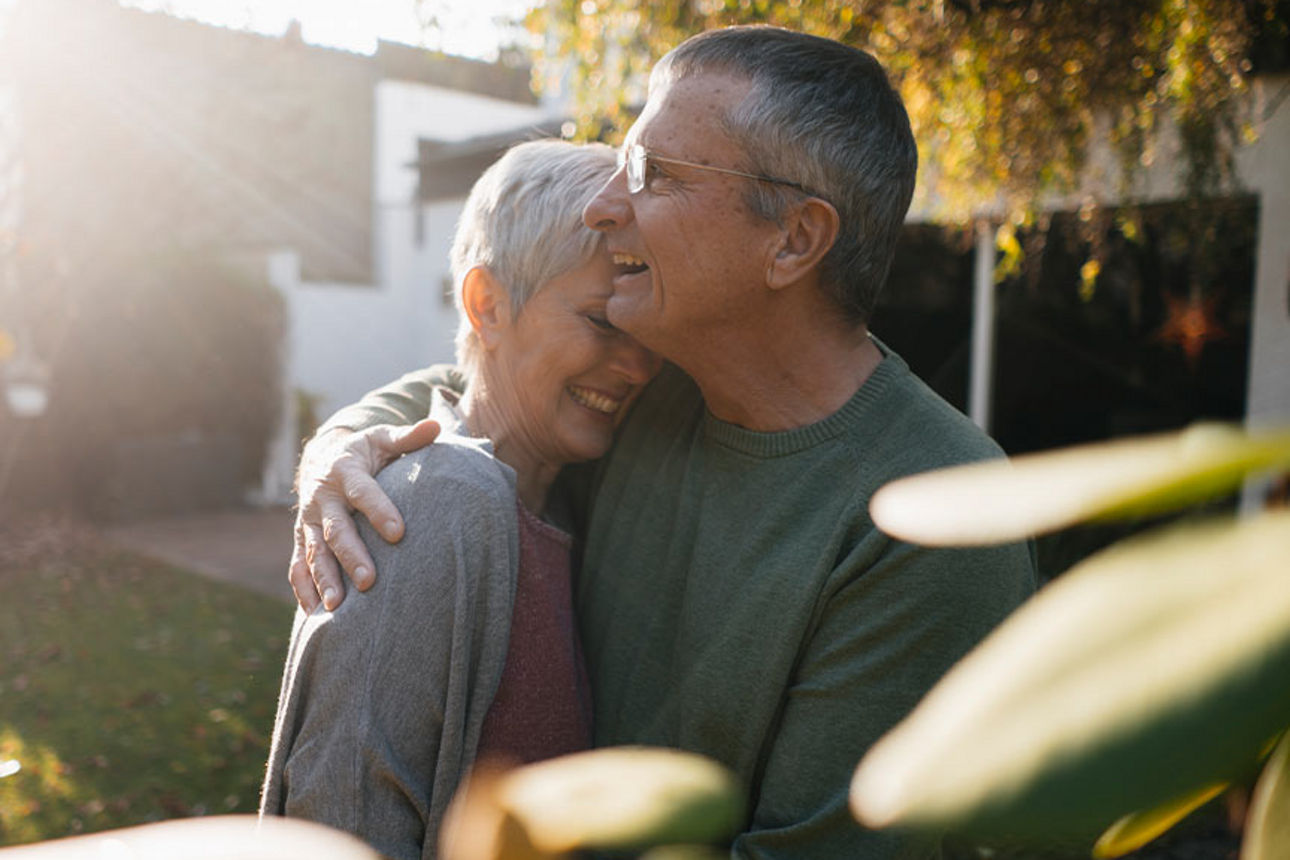 Ein älteres Paar liegt sich in den Armen im Garten vor ihrem Haus.