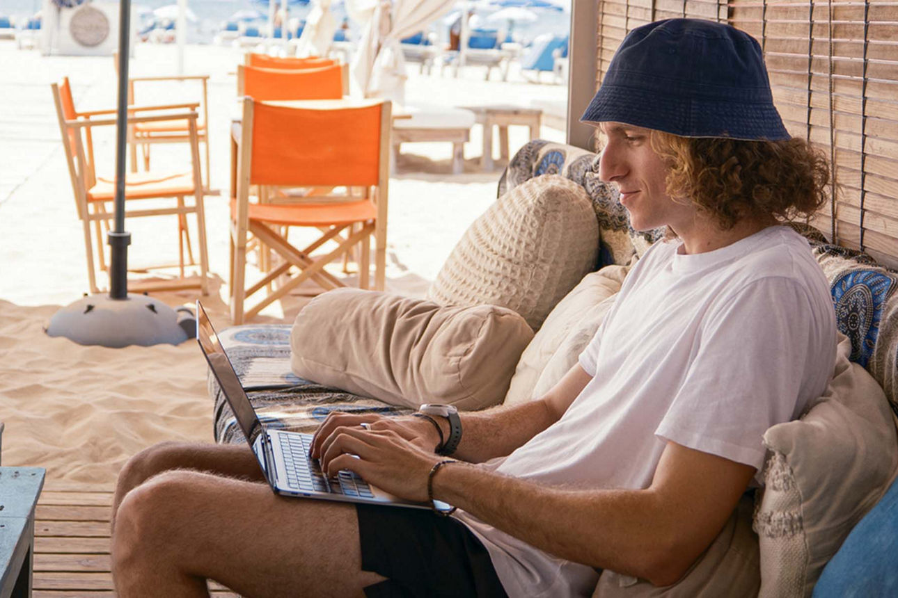 Junger Mann mit Laptop am Strand