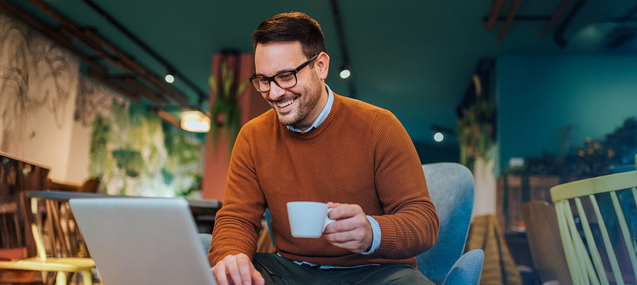 Junger Mann sitzt in einem Café vor seinem Laptop