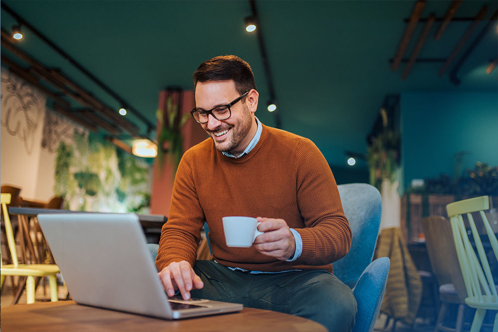 Junger Mann sitzt in einem Café vor seinem Laptop