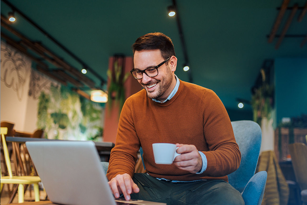 Junger Mann mit Tasse Kaffee am Laptop