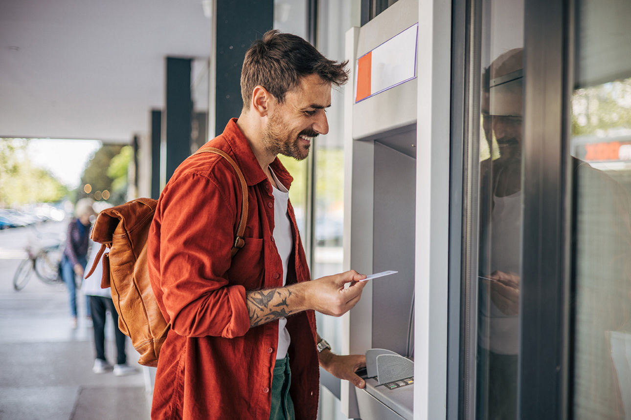 Mann steht am Geldautomaten und will seine Karte gerade einstecken