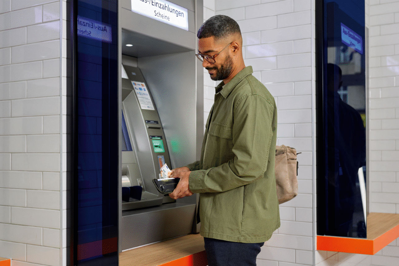 Mann hebt Geld an einem VR Bank Automaten ab.