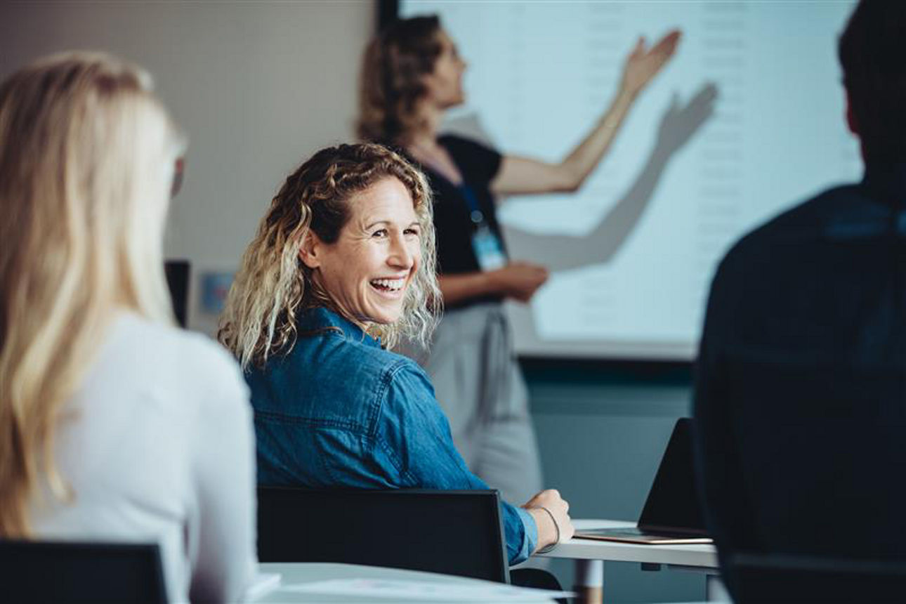 Junge Frau lehnt sich in einerm Seminar zurück und lacht