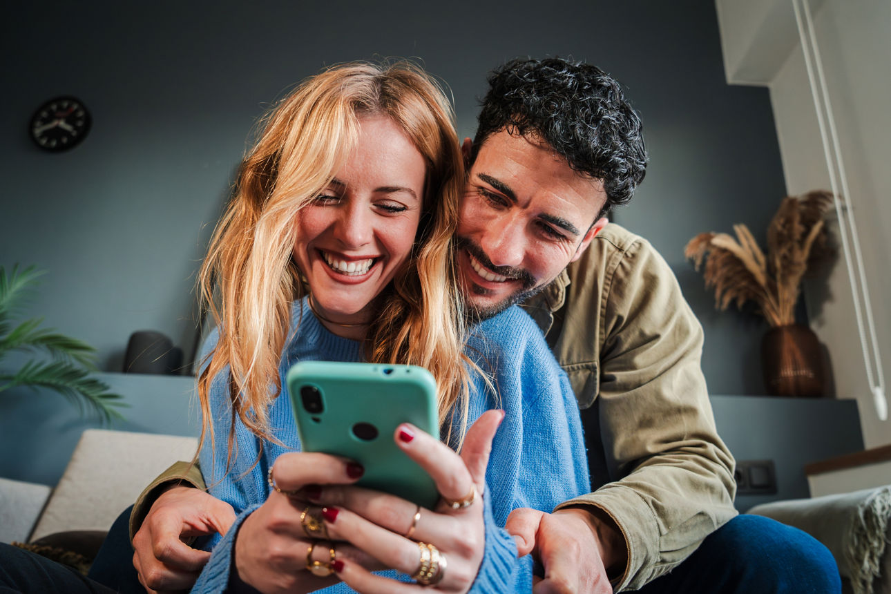 2205860288 Young caucasian couple smiling using a cellphone to do shopping online. Man and woman watching the social media with a smartphone. Adult friends having fun browsing on internet with a mobile phone. High quality photo