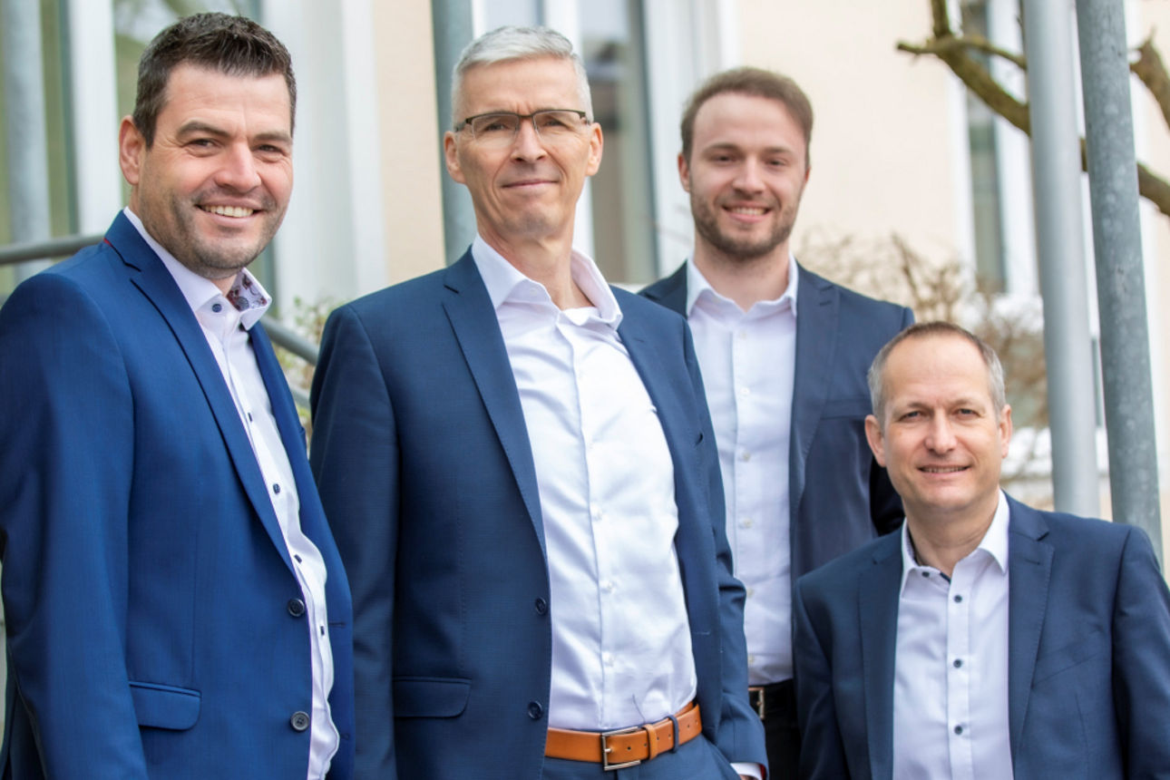 Vier Männer vor einem Haus zwischen zwei Bäumen