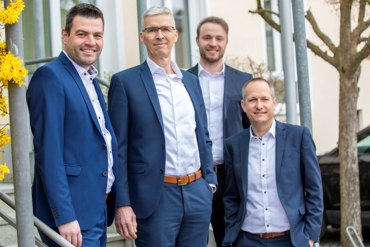 Vier Männer vor einem Haus zwischen zwei Bäumen