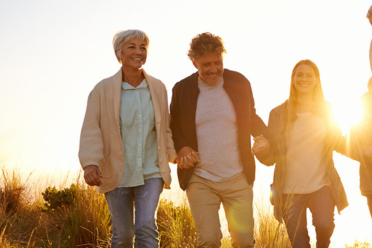 Mehrere Personen unterschiedlicher Generationen gehen gemeinsam im Sonnenlicht über eine Wiese und symbolisieren familiäre Verbundenheit.