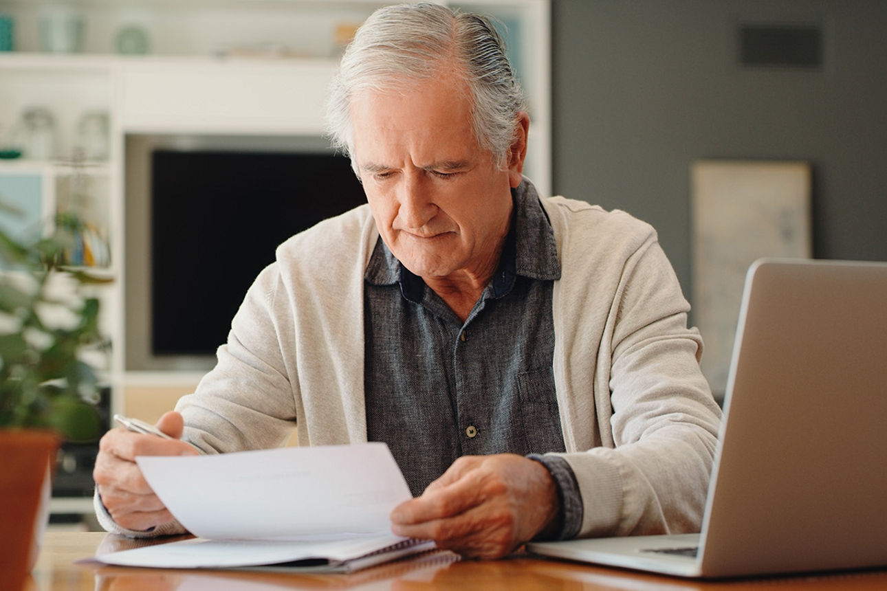 Älterer Mann sitzt am Tisch und liest einen Brief