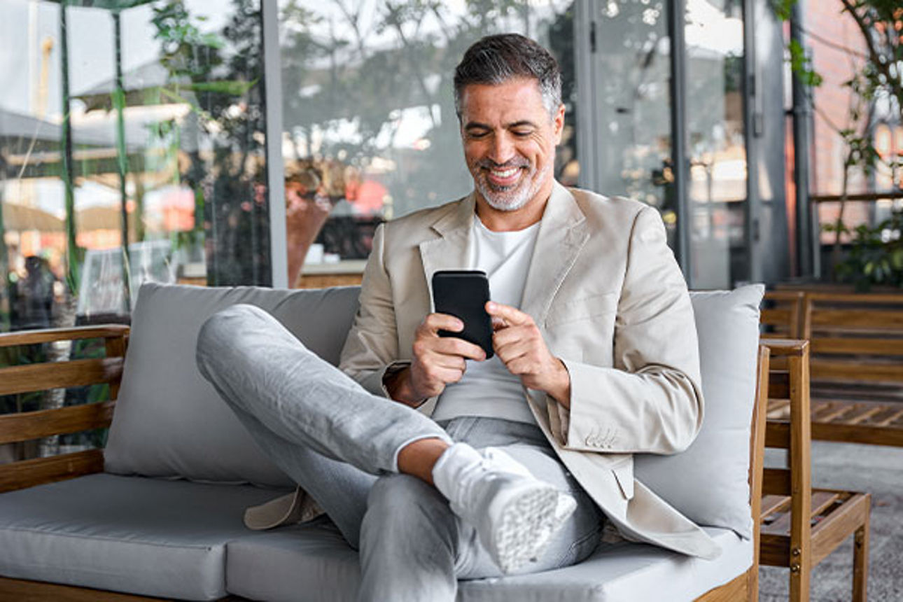 Mann sitzt entspannt in einem Sessel und schaut lächelnd auf sein Smartphone