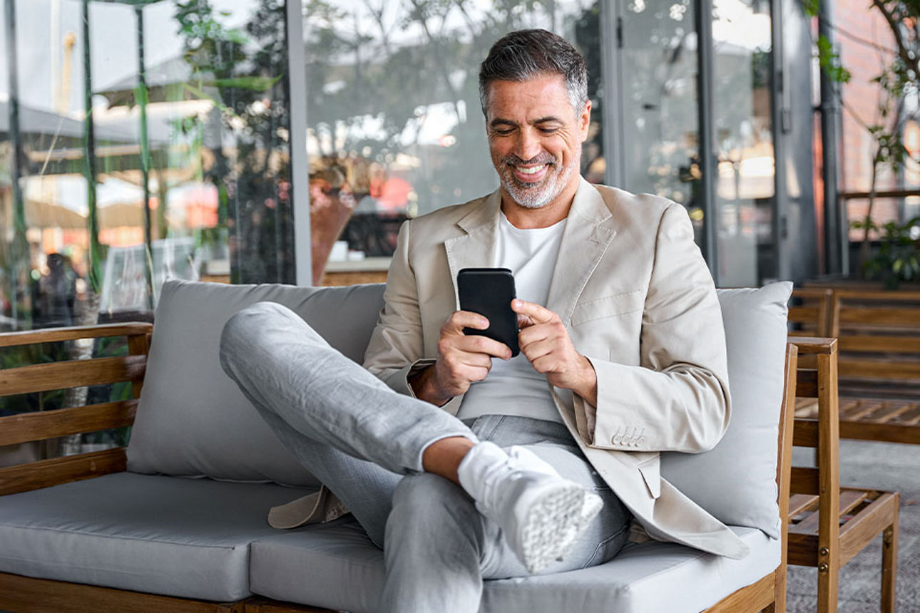 Ein Mann sitzt auf einem Sofa und schaut lächelnd in sein Smartphone