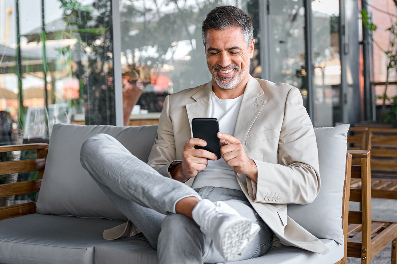Mann sitzt entspannt in einem Sessel und schaut lächelnd auf sein Smartphone