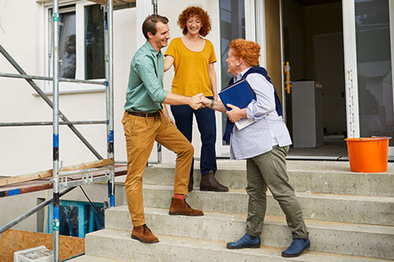 Lächelndes Paar mit einer Beraterin bei der Immobilienbesichtigung vor einem Haus