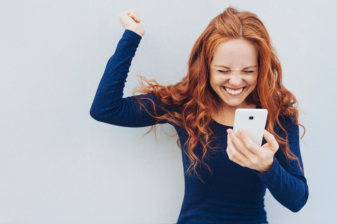Eine Frau, die ein Handy in der Hand hält und jubelt.