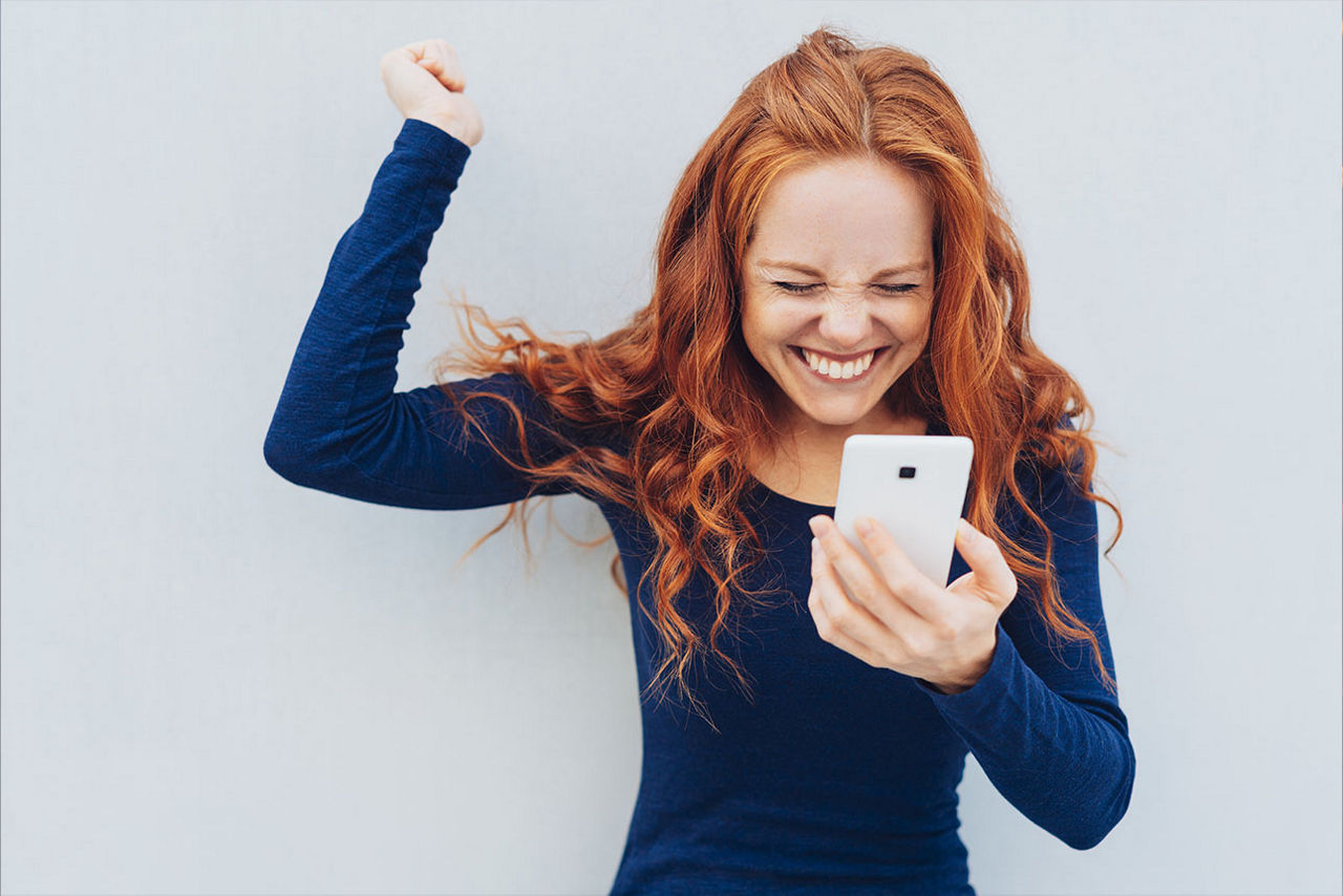 Eine Frau mit Handy in der Hand jubelt