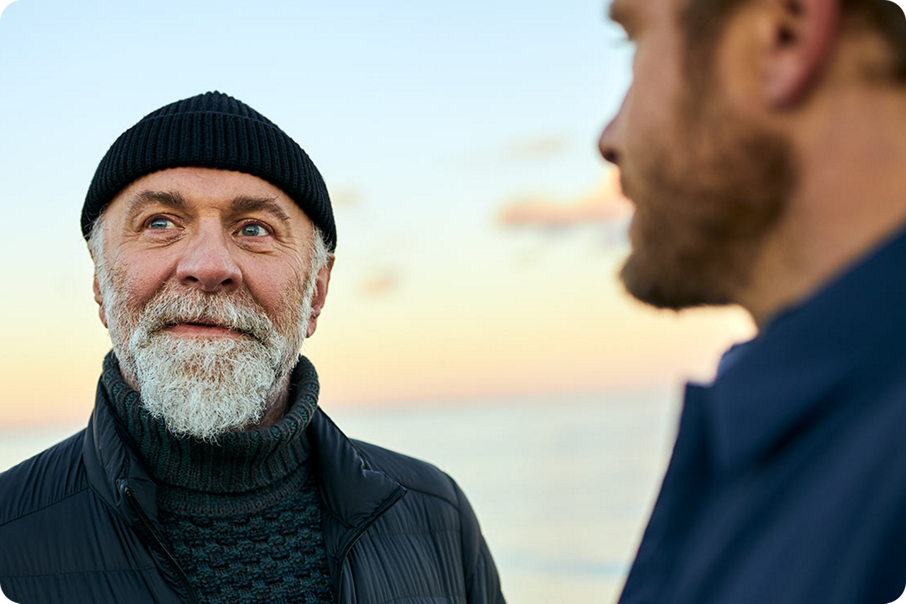 Zwei Männer stehen vor dem Meer und sprechen miteinander
