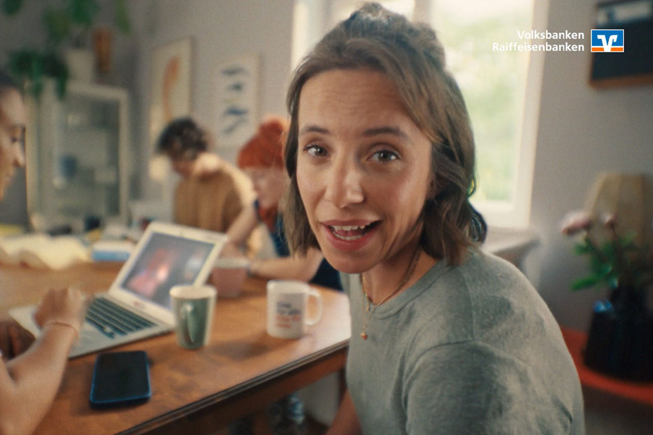 Vier junge Menschen sitzen fröhlich auf einer Couch und halten sich an den Händen