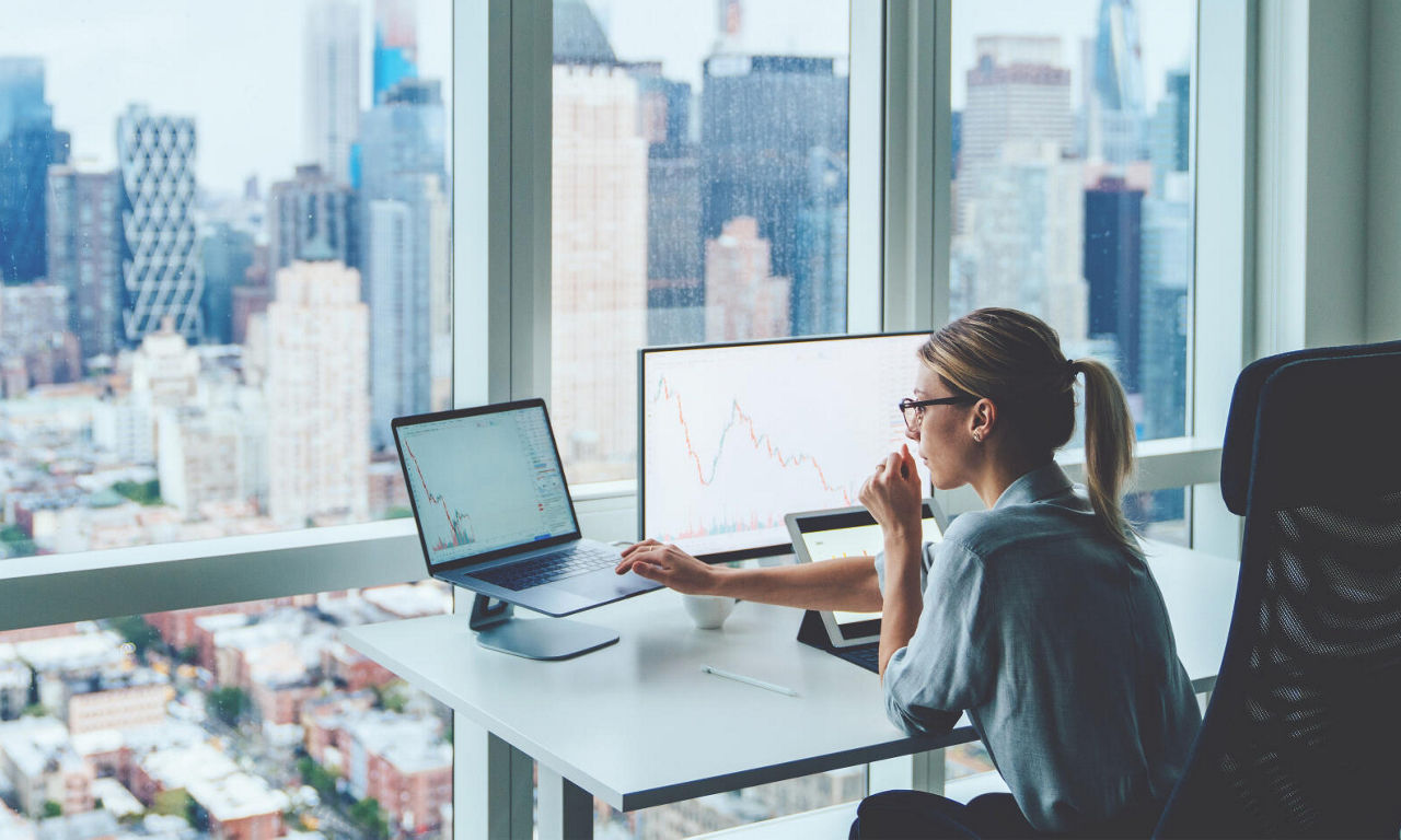 Business Frau sitz am Schreibtisch und schaut auf Ihre Monitore.