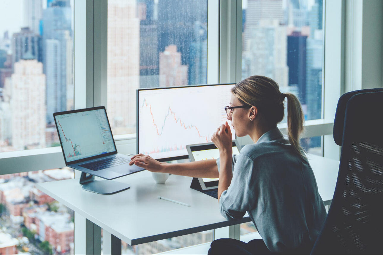 Business Frau sitz am Schreibtisch und schaut auf Ihre Monitore.