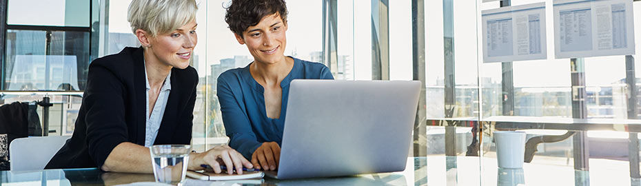 Zwei Frauen sitzen an einem Tisch und arbeiten gemeinsam an einem Laptop