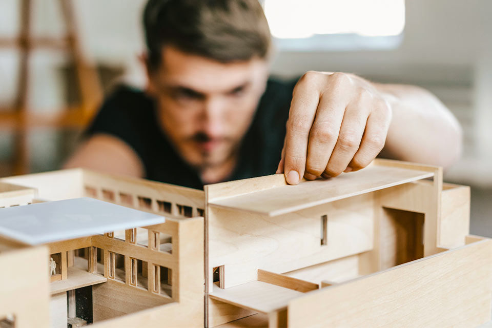 Ein Mann baut ein Modell von einem Haus aus Holz.