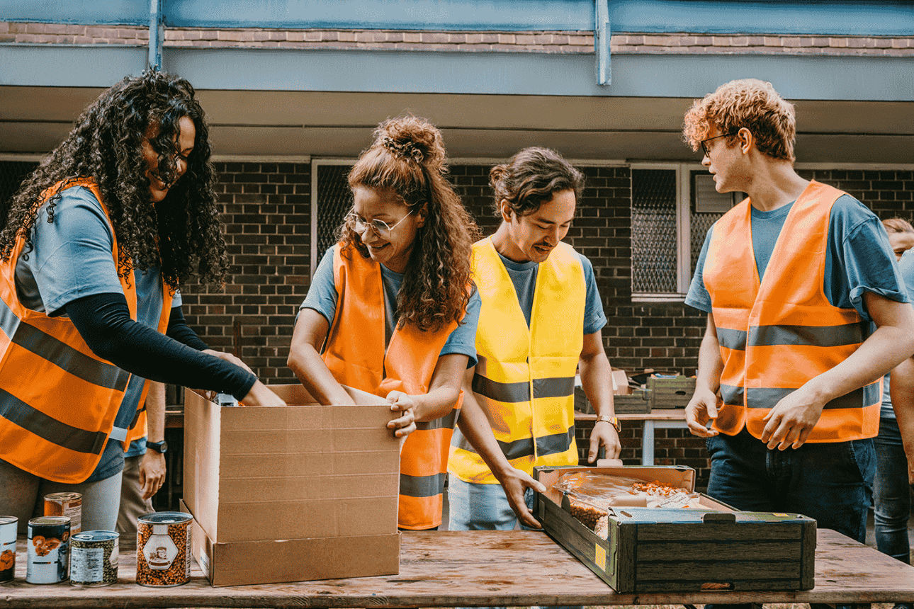 Vier Personen in Warnwesten packen Lebensmittel in Kartons – Einsatz für soziales Engagement.