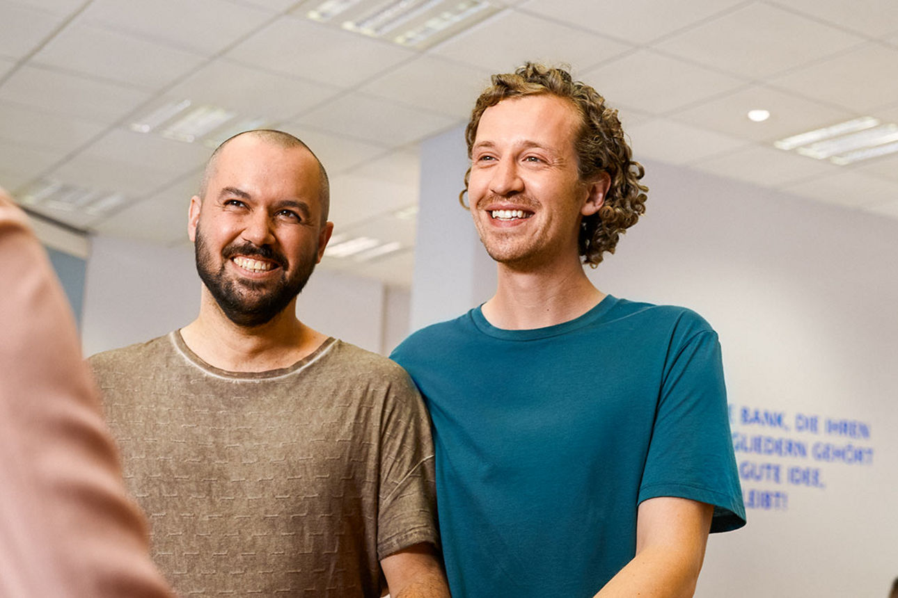 Zwei lächelnde Männer im Beratungsgespräch vor einem Bankschalter