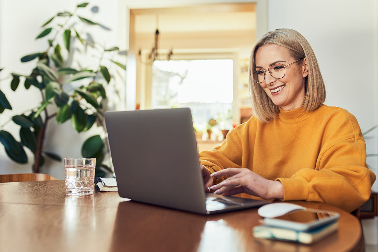 Eine Frau arbeitet lächelnd an ihrem Laptop