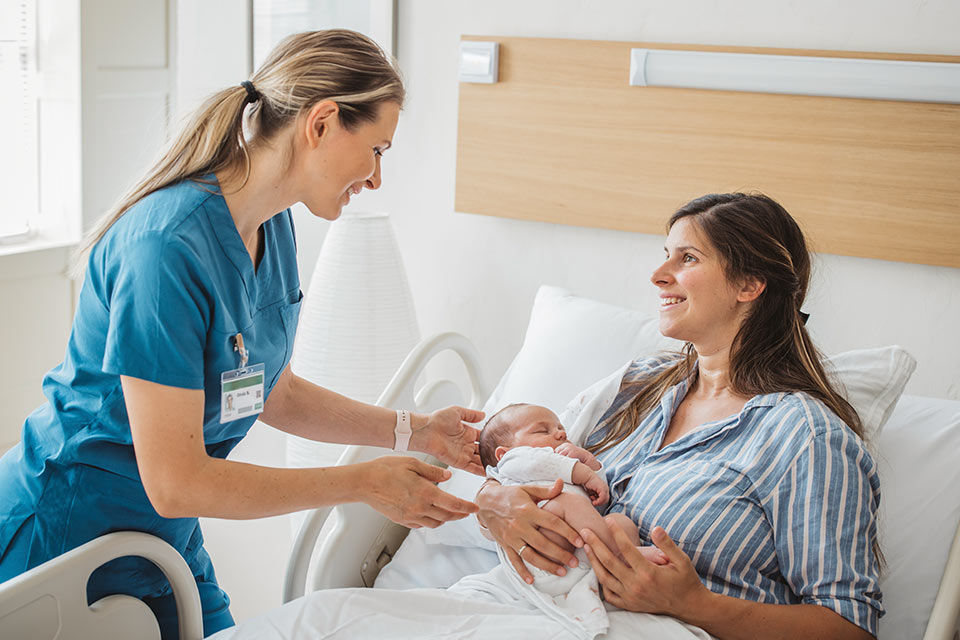 Eine Krankenschwester kümmert sich um eine junge Mutter mit Neugeborenem