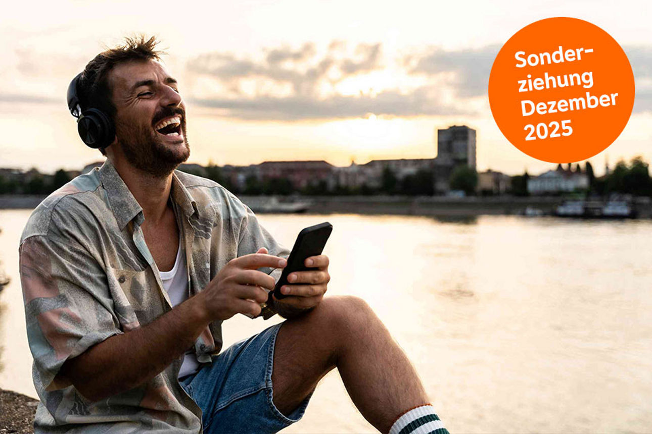 Mann sitzt mit Handy und Kopfhörern am Fluss