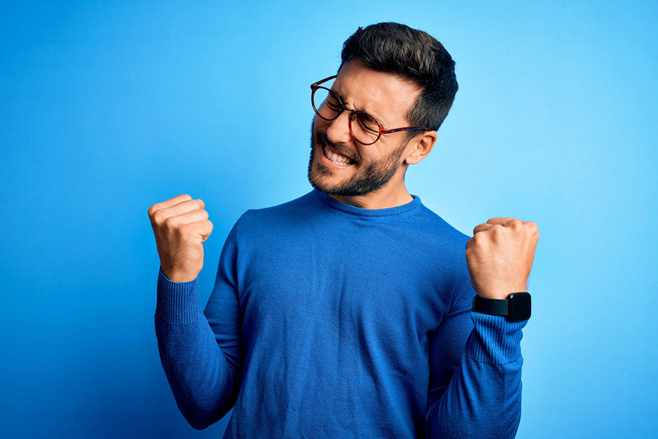 Mann mit Brille und blauem Pulli kneift die Augen zu und drückt beide Daumen.
