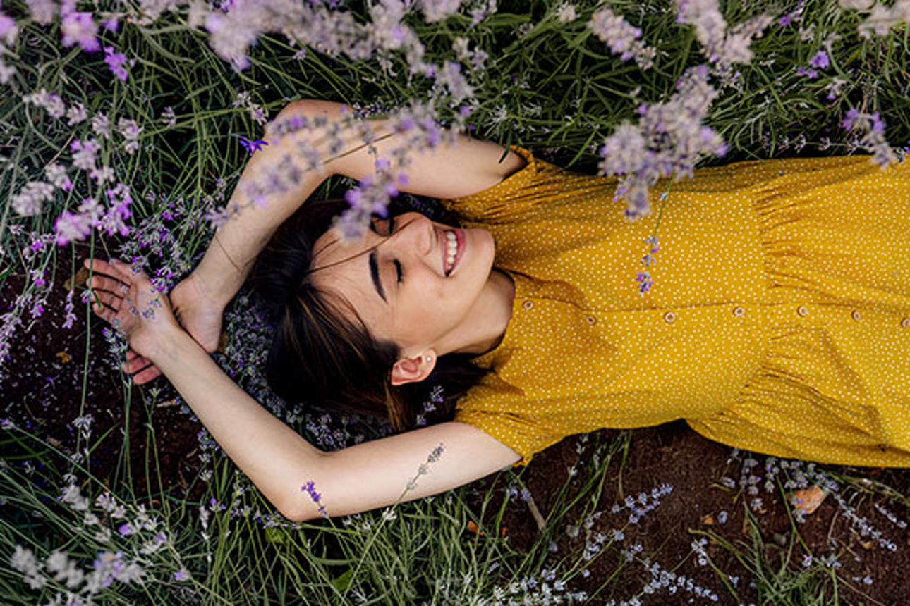 Junge Frau liegt träumend auf einer Blumenwiese.