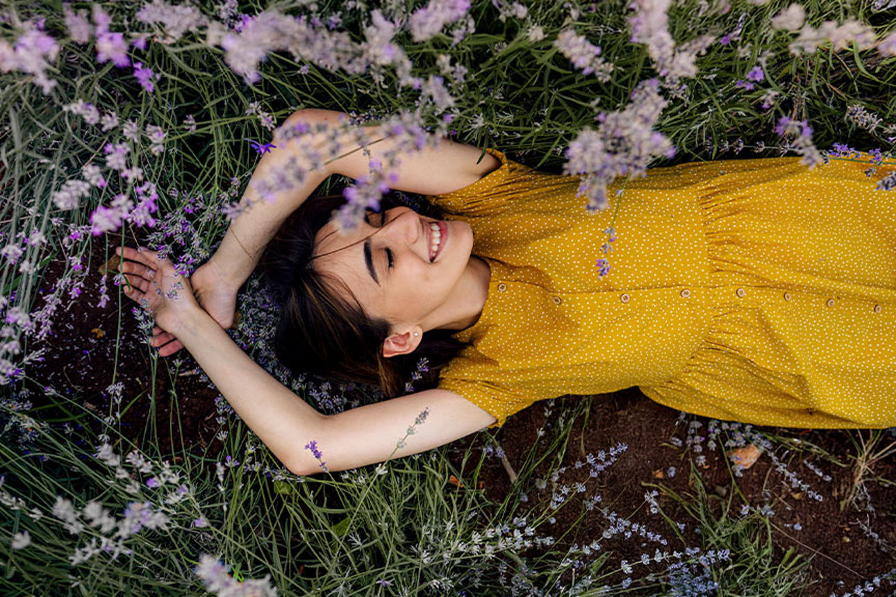 Eine junge Frau in einem gelben Kleid liegt in einem Lavendelfeld.