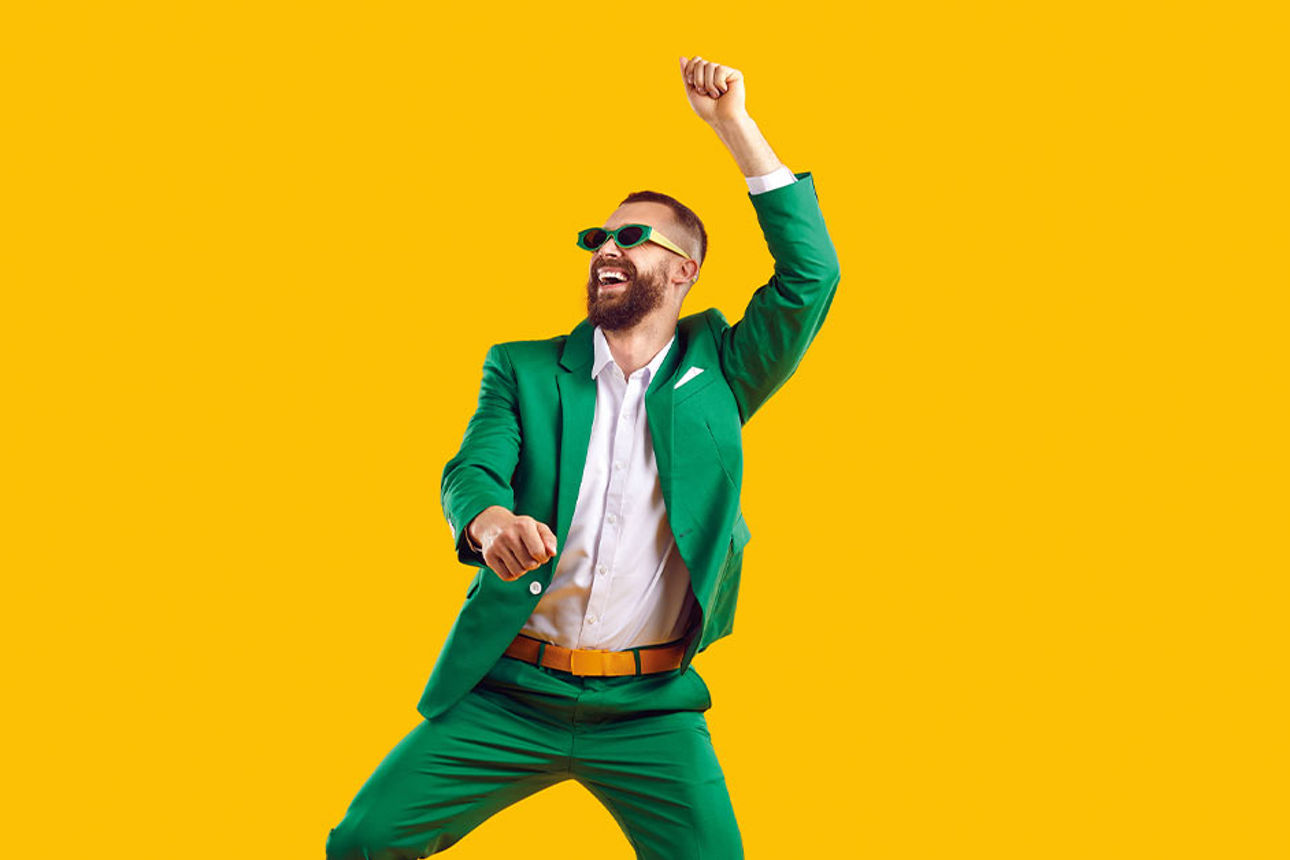 Mann feiernd in grünem Anzug vor gelber Wand