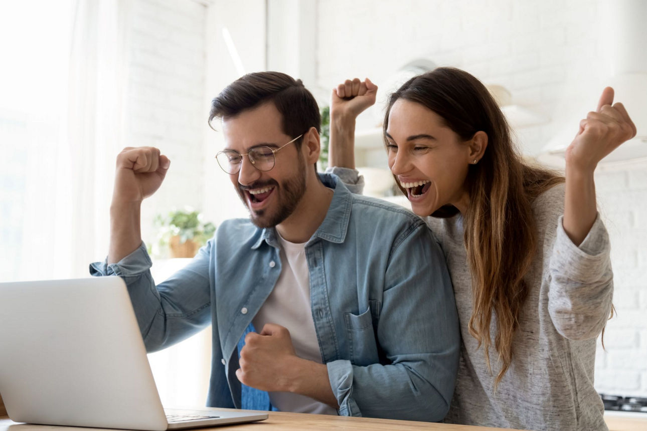 Pärchen sitzt zusammen vor dem Laptop und jubelt über den Gewinn der Gewinnsparlose