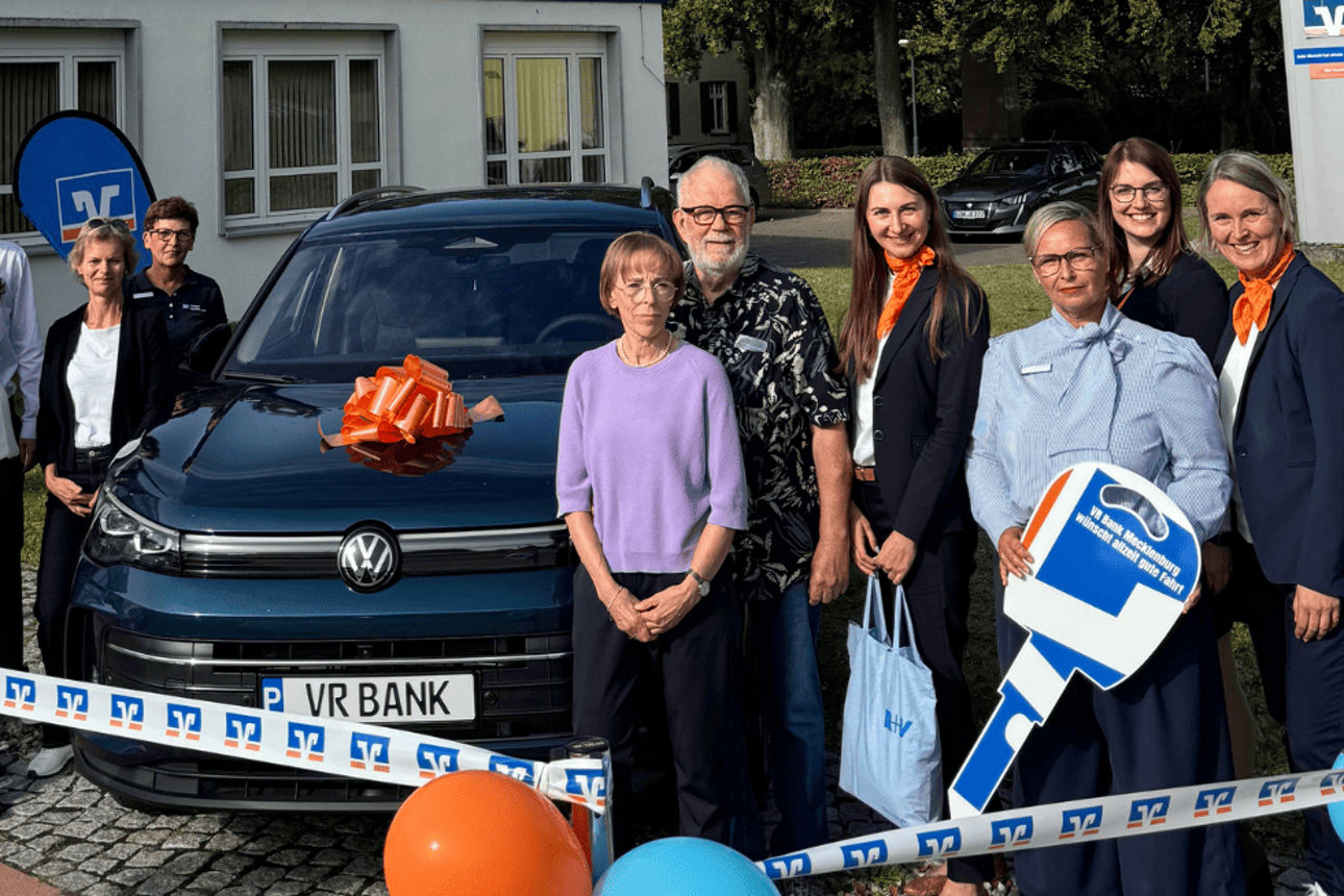 Ehepaar steht mit VR-Bank-Mitarbeitern vor einem gewonnen VW Tiguan eHybrid