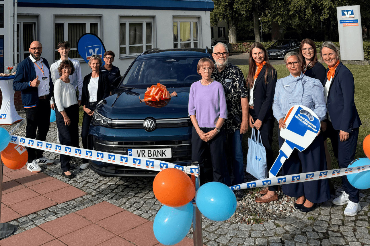 Ehepaar steht mit VR-Bank-Mitarbeitern vor einem gewonnen VW Tiguan Hybrid